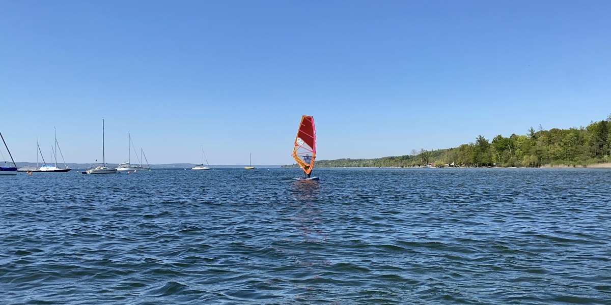 Ein Surfer mit rotem Segel auf dem Starnberger See. Im Hintergrund sind mehrere Segelboote zu sehen., © Wassersportcenter Starnberger See, Foto: Wallusch Ein Surfer mit rotem Segel auf dem Starnberger See. Im Hintergrund sind mehrere Segelboote zu sehen., © Wassersportcenter Starnberger See, Foto: Wallusch