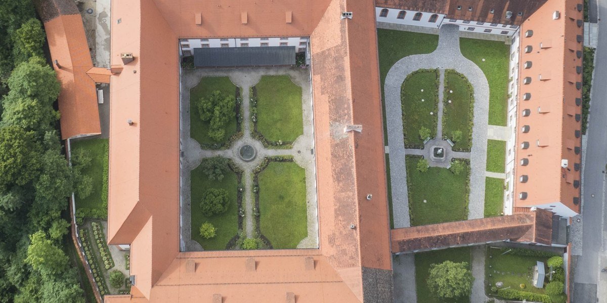 Das Kloster Beuerberg aus der Vogelperspektive
Der historische Klosterkomplex mit roten Ziegeldächern umschließt zwei große Innenhöfe mit symmetrischen Gartenanlagen. Das Gesamtbild zeigt eine klare, symmetrische Architektur und gepflegte Grünflächen., © Kloster Beuerberg|Foto: Christian Schmid Das Kloster Beuerberg aus der Vogelperspektive
Der historische Klosterkomplex mit roten Ziegeldächern umschließt zwei große Innenhöfe mit symmetrischen Gartenanlagen. Das Gesamtbild zeigt eine klare, symmetrische Architektur und gepflegte Grünflächen., © Kloster Beuerberg|Foto: Christian Schmid