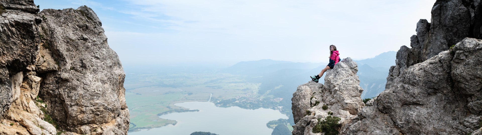 Eine Bergsteigerin sitzt auf einem Felsen und im Hintergrund ist der Kochelsee zu sehen, © Tourist Information Kochel a. See, Fotograf Matthias Fend Eine Bergsteigerin sitzt auf einem Felsen und im Hintergrund ist der Kochelsee zu sehen, © Tourist Information Kochel a. See, Fotograf Matthias Fend