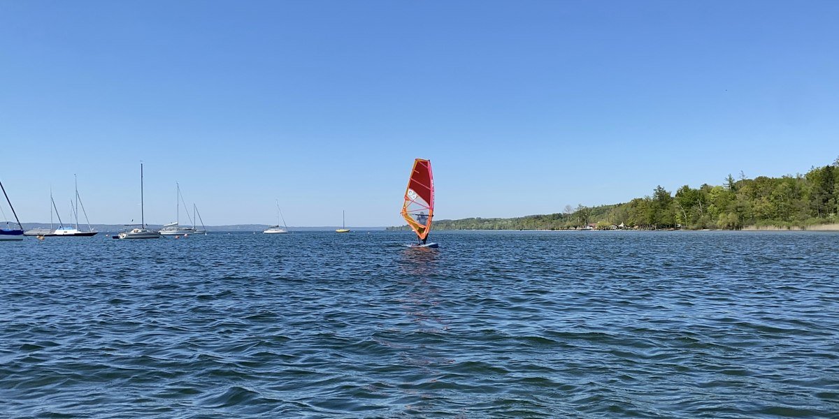 Ein Surfer mit rotem Segel auf dem Starnberger See. Im Hintergrund sind mehrere Segelboote zu sehen., © Wassersportcenter Starnberger See, Foto: Wallusch Ein Surfer mit rotem Segel auf dem Starnberger See. Im Hintergrund sind mehrere Segelboote zu sehen., © Wassersportcenter Starnberger See, Foto: Wallusch
