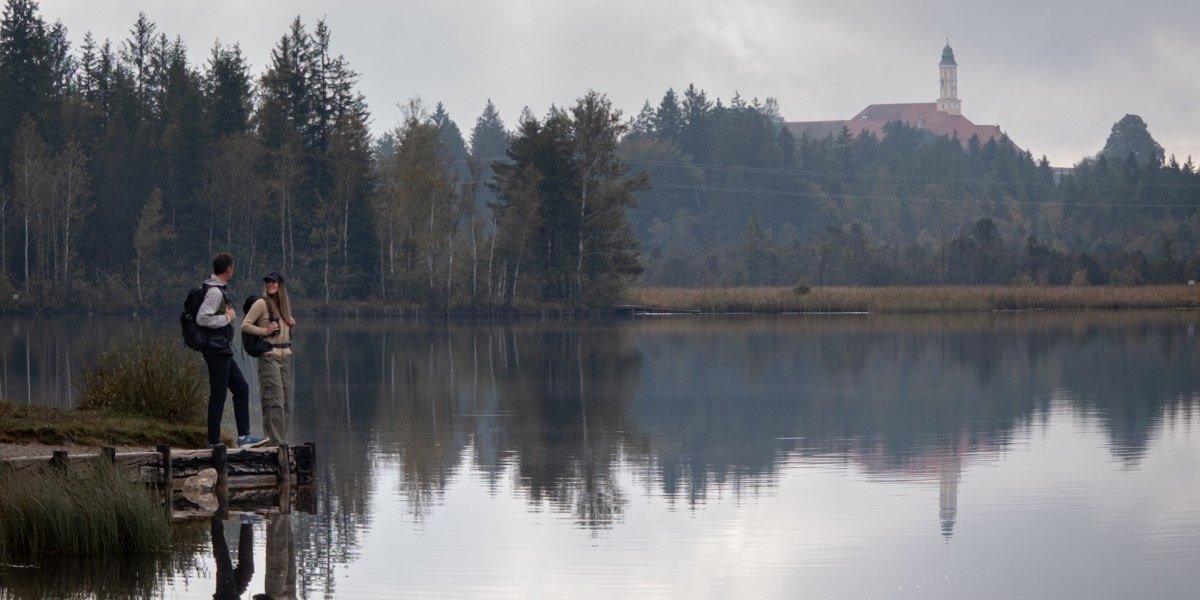 Zwei Wanderer genießen den Blick auf Kloster Reutberg oberhalb des Kirchsees, © Tölzer Land Tourismus|Christian Geigl Zwei Wanderer genießen den Blick auf Kloster Reutberg oberhalb des Kirchsees, © Tölzer Land Tourismus|Christian Geigl