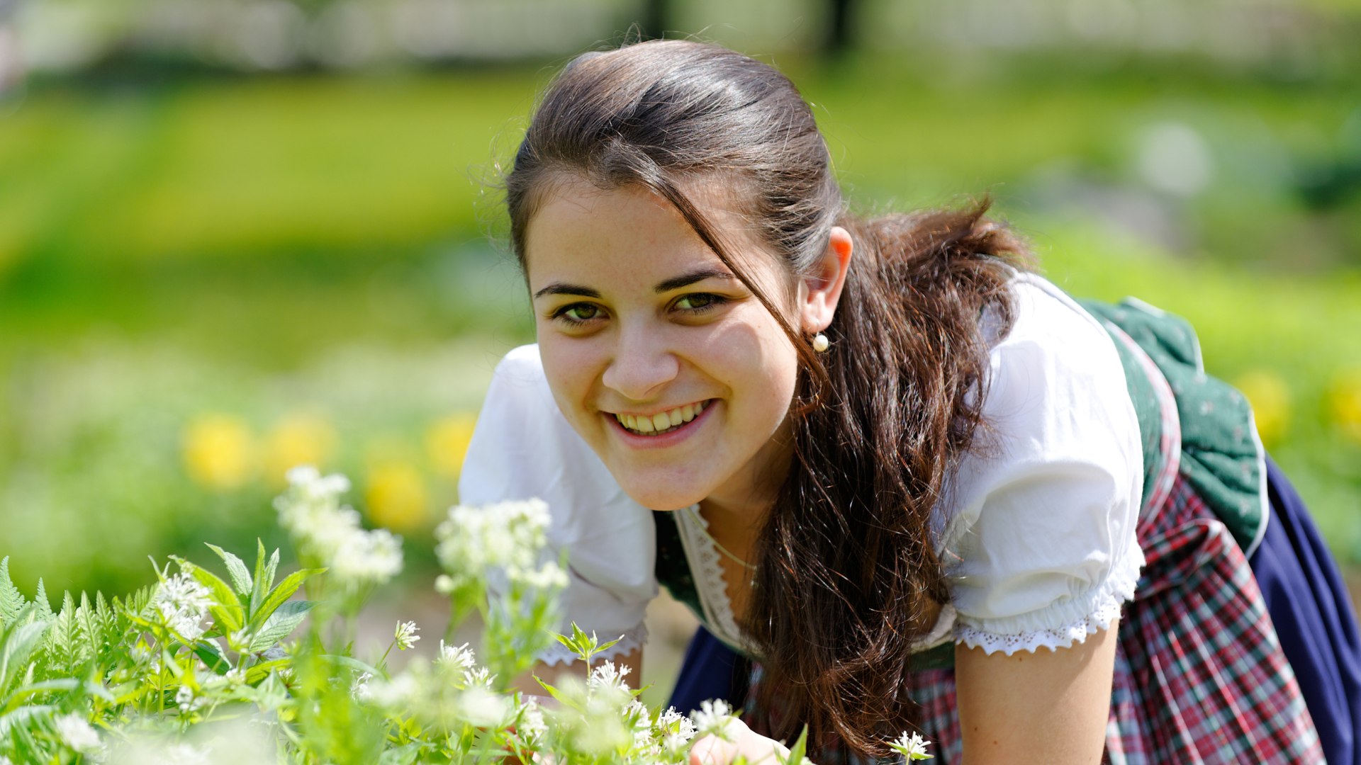 Eine im Dirndl gekleidete junge Frau beugt sich zu weißen Blüten., © Gästeinformation Bad Heilbrunn Eine im Dirndl gekleidete junge Frau beugt sich zu weißen Blüten., © Gästeinformation Bad Heilbrunn