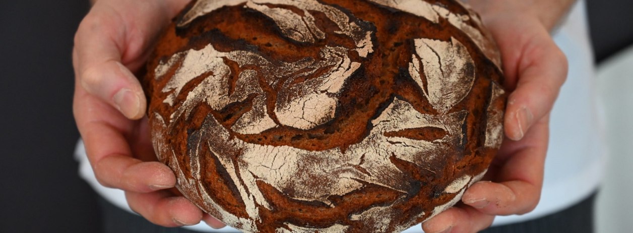 Bäcker, Metzger, das Handwerk - ohne sie alle wäre der Tourismus nicht das, was er ist. Das Bild zeigt einen Laib Brot mit dunkler Kruste in den Händen eines Bäckers., © Kerstin Riemer Bäcker, Metzger, das Handwerk - ohne sie alle wäre der Tourismus nicht das, was er ist. Das Bild zeigt einen Laib Brot mit dunkler Kruste in den Händen eines Bäckers., © Kerstin Riemer