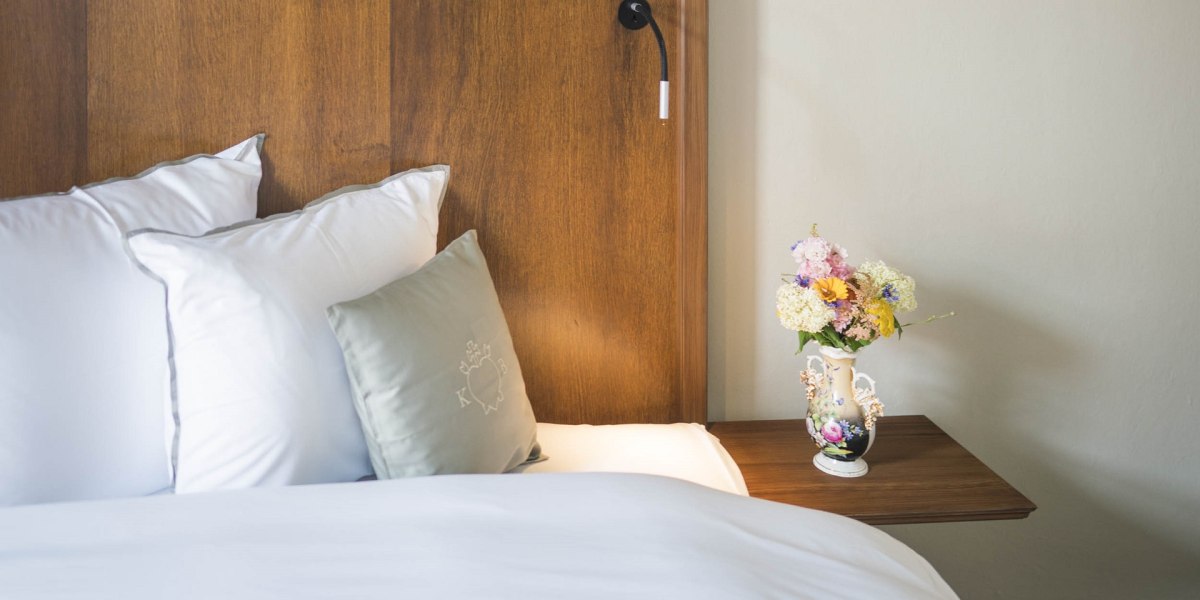 Gute gebettetist man in den stilvoll eingerichteten Zimmern im Kloster Beuerberg.
Das Bild zeigt ein helles Schlafzimmer mit Holzvertäfelung am Kopfteil des Betts, darauf ein lateinisches Bibelzitat. Weiße Bettwäsche mit einem grauen Zierkissen. Rechts daneben ein schwebender Nachttisch mit bunter Blumenvase. , © Kloster Beuerberg|Foto: Christian Schmid Gute gebettetist man in den stilvoll eingerichteten Zimmern im Kloster Beuerberg.
Das Bild zeigt ein helles Schlafzimmer mit Holzvertäfelung am Kopfteil des Betts, darauf ein lateinisches Bibelzitat. Weiße Bettwäsche mit einem grauen Zierkissen. Rechts daneben ein schwebender Nachttisch mit bunter Blumenvase. , © Kloster Beuerberg|Foto: Christian Schmid