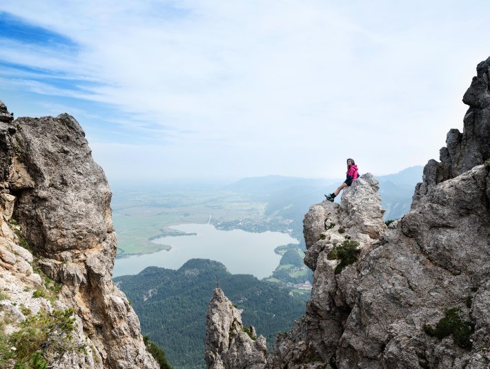 Eine Bergsteigerin sitzt auf einem Felsen und im Hintergrund ist der Kochelsee zu sehen, &copy; Tourist Information Kochel a. See, Fotograf Matthias Fend