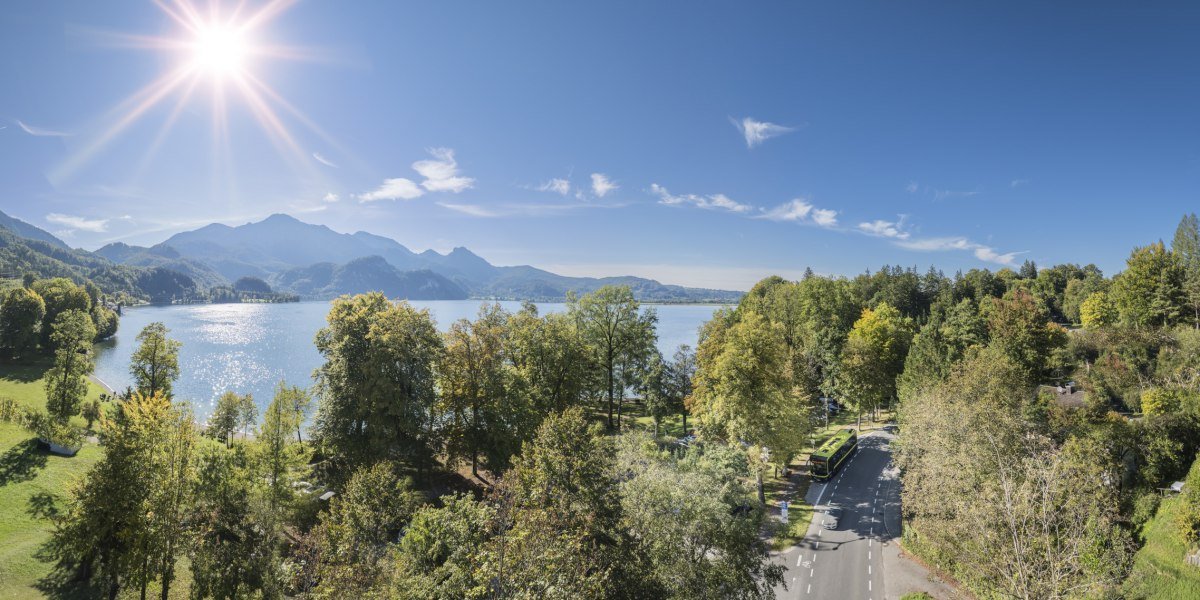 Sonniger Herbsttag am Walchensee mit glitzerndem Wasser, gr&uuml;nen und gelben B&auml;umen, Bergen im Hintergrund und einem Bus auf der Stra&szlig;e rechts im Bild., &copy; Landratsamt Bad T&ouml;lz-Wolfratshausen|Dietmar Denger