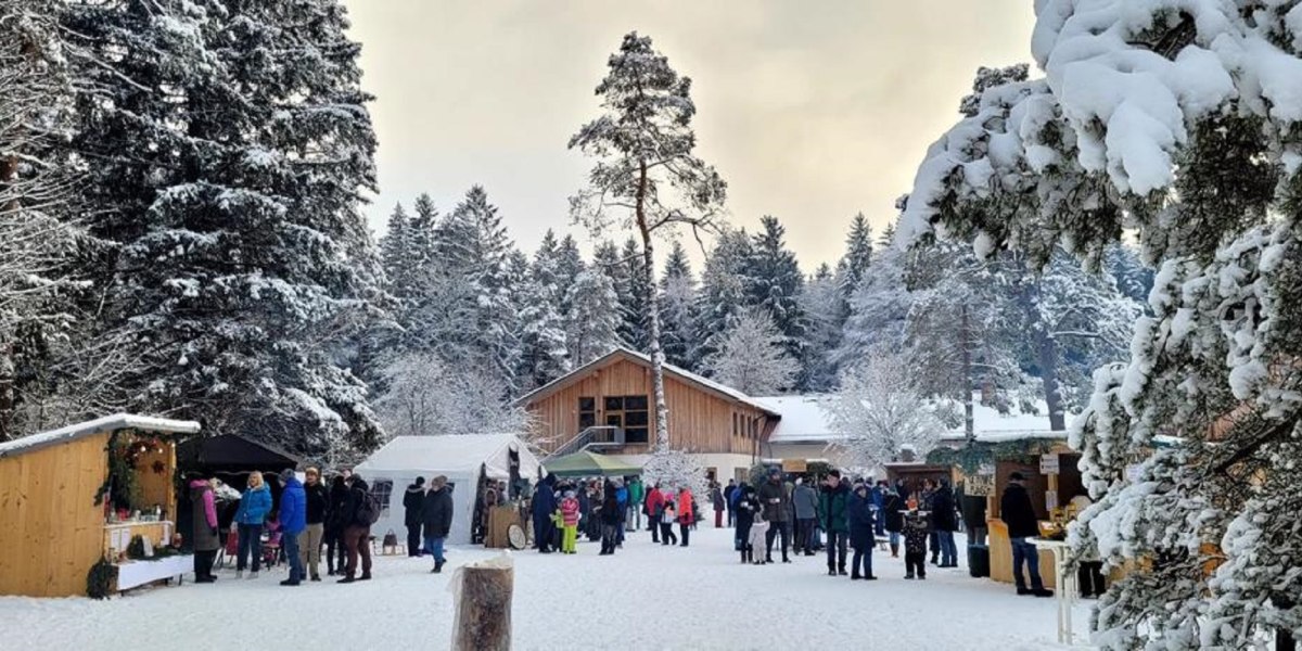 Das Bild zeigt einen winterlichen Weihnachtsmarkt im Wald mit mehreren St&auml;nden und vielen Besuchern, &copy; Jugendsiedlung Hochland, K&ouml;nigsdorf