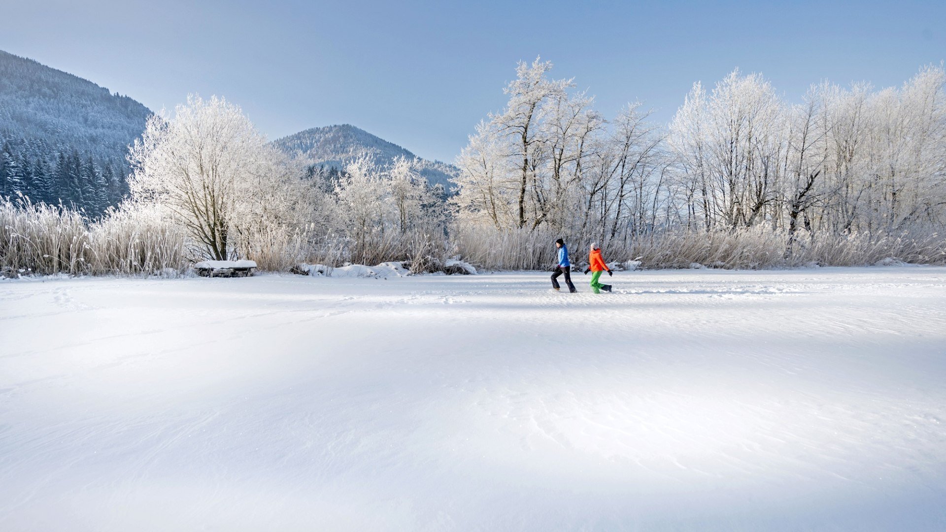 Zwei Frauen in bunter Winterkelidung stapfen durch die tiefverschneite Winterlandschaft, © Tourismus Oberbayern München/Peter von Felbert