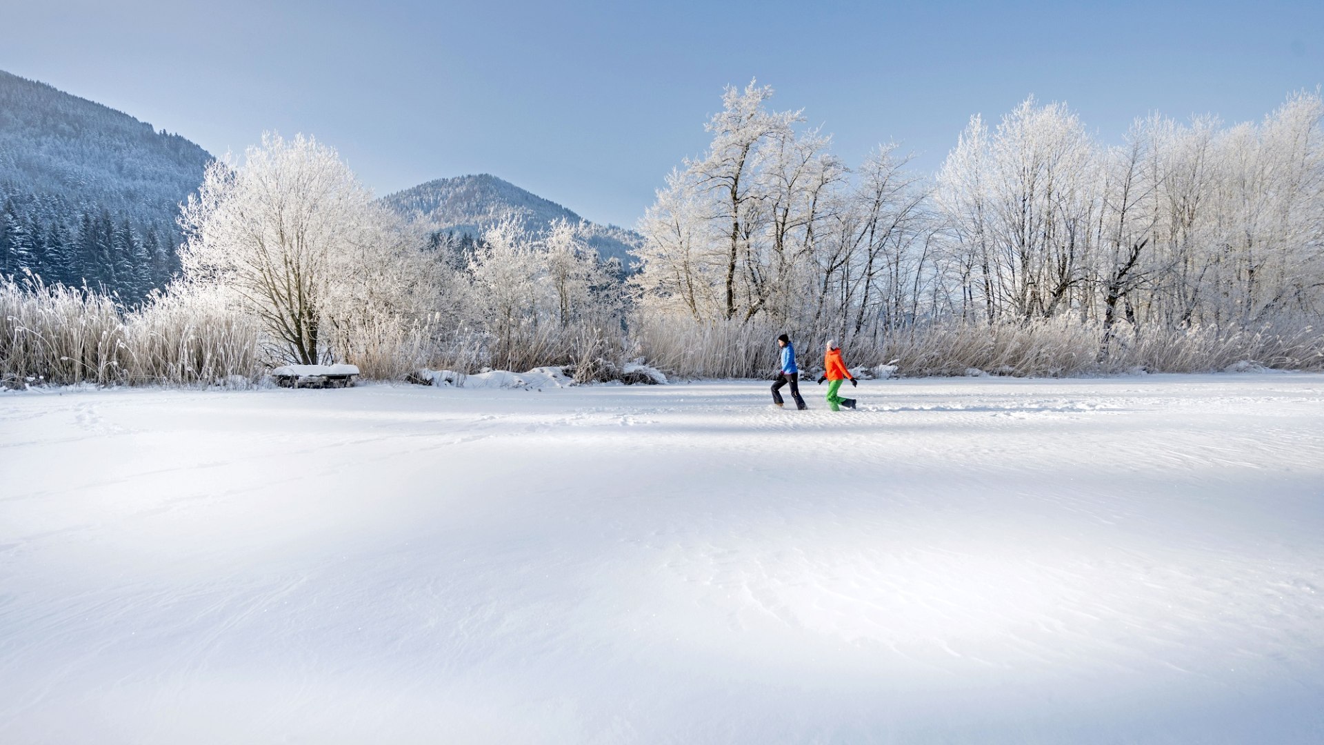 Zwei Frauen in bunter Winterkelidung stapfen durch die tiefverschneite Winterlandschaft, © Tourismus Oberbayern München/Peter von Felbert