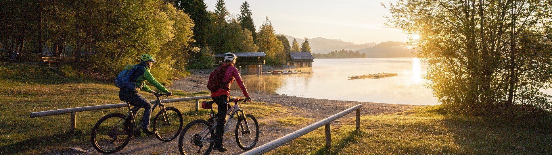 Welch Ausblick auf den Walchensee! Zwei Fahrradfahrer fahren auf den in morgendlichen Sonnenlicht getauchten Walchensee zu., © Archiv Tölzer Land Tourismus| Foto: Bernd Ritschel