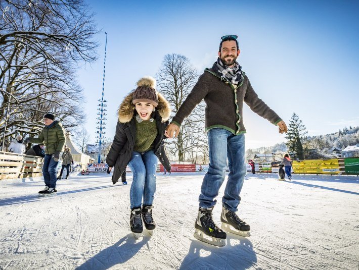 Auf der Eisfläche von Wolfratshausen laufen fröhliche Menschen mit Schlittschuhen über das Eis., © Stadt Wolfratshausen | Adrian Greiter