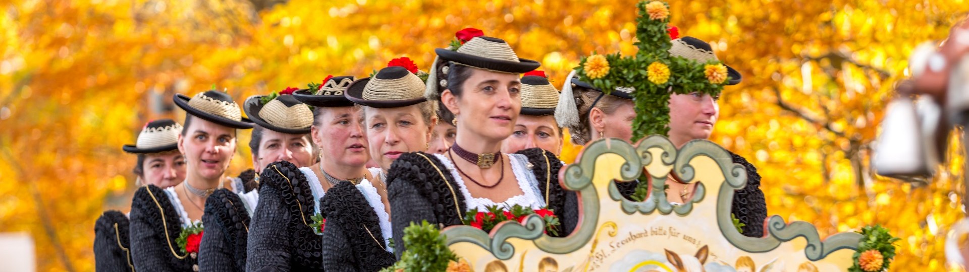 Pr&auml;chtig geschm&uuml;ckte Pferdegespanne und Frauen in Tracht bei der Wallfahrt zu Ehren des Hl. Leonhard in Bad T&ouml;lz vor B&auml;umen, die golden vom Herbstlaub leuchten, &copy; T&ouml;lzer Land Tourismus|Harald K&uuml;bler