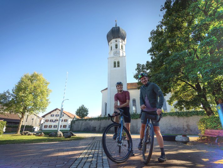 Zwei Fahrradfahrer pausieren vor der barocken St.Benediktkirche in Geretsried Gelting mit seinem markanten Zweibelturm, &copy; Stadt Geretsried|Farmhouse 7