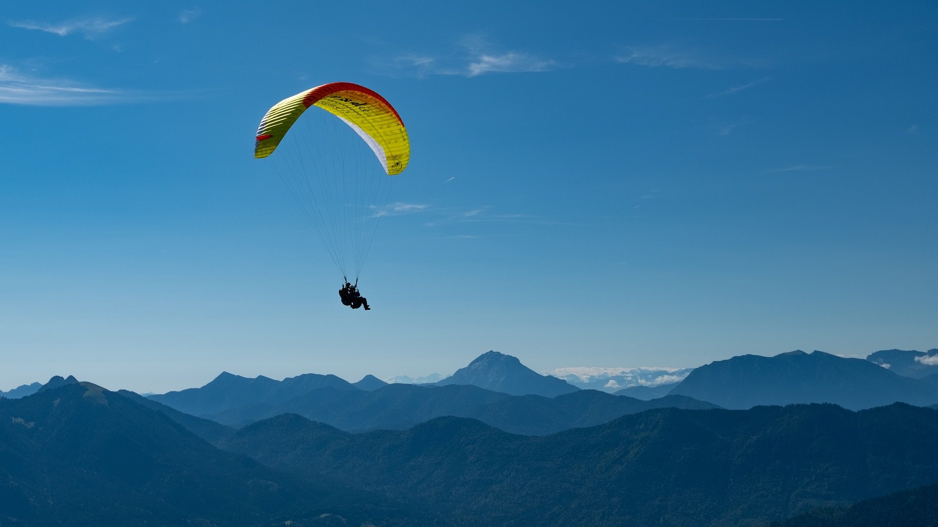 Ein tolles Erlebnis- Gleitschirmfliegen.
Das Bild zeigt einen Gleitschirmflieger &uuml;ber blauen Bergk&auml;mmen; im Hintergrund schneebedeckte Alpen unter klarem Himmel., &copy; Adventure Sports Gbr|Foto: Rafael Frei