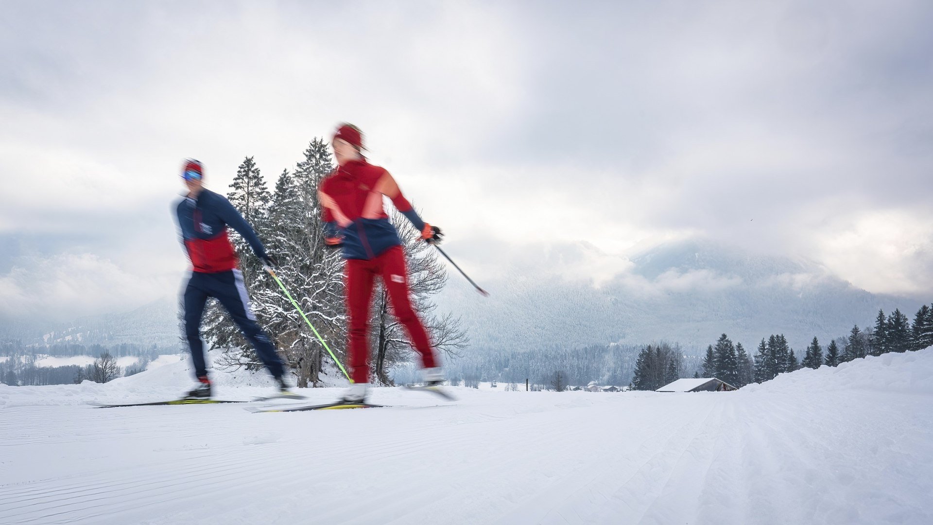 Zwei Langl&auml;ufer in roter und blauer Sportkleidung fahren bei winterlichem Bergpanorama auf einer gespurten Loipe durch verschneite Landschaft., &copy; T&ouml;lzer LAnd TourismusIDietmar Denger