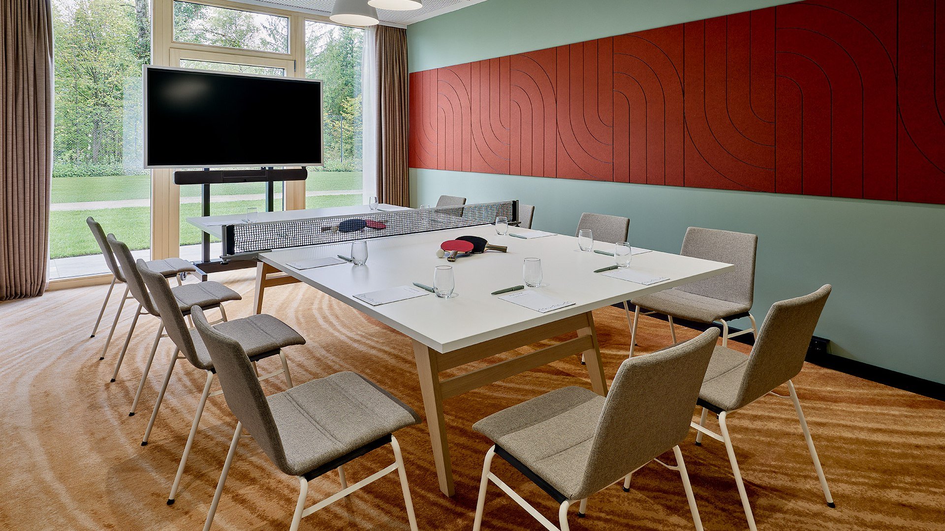 Ideale R&auml;umlichkeit f&uuml;r kleine Tagungen, Schulungen, Meetings wie hier im Raum "Florihang" des Flesslers Lenggries gibt es im T&ouml;lzer Land.
Das Bild zeigt einen Tagungsraum mit gro&szlig;er Fensterfront, davor ein TV-Screen. Die Wand ist zart gr&uuml;n mit einem breiten dunkelroten Blockstreifen. In der Raummitte ist ein wei&szlig;er Tisch mit hellen St&uuml;hlen., &copy; Flesslers Lenggries, Tribute Portfolio Marriott, Foto: Matthias Hamel